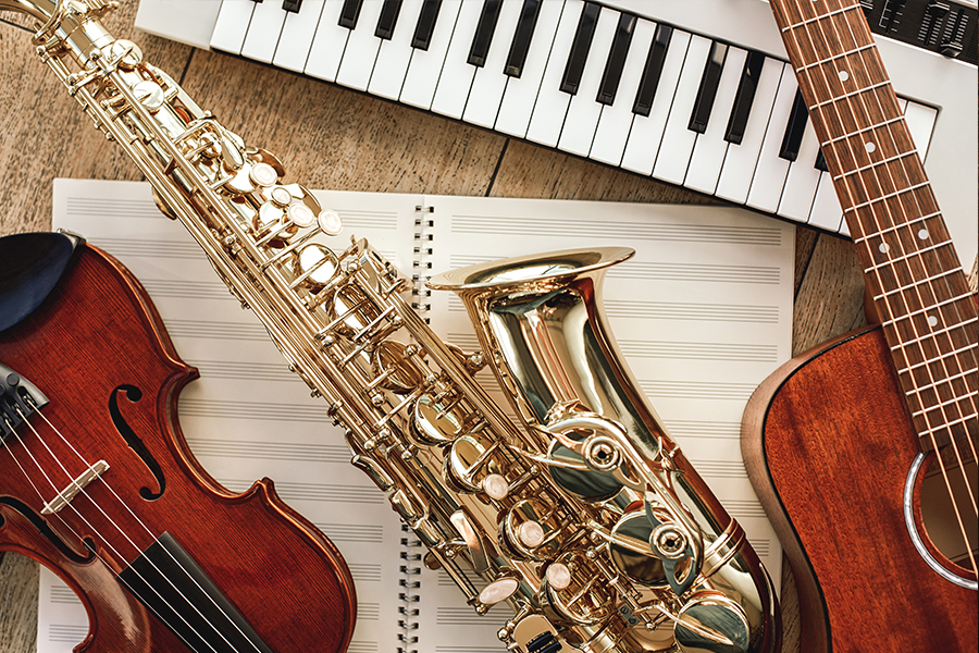 Overhead view of a violin, saxophone, guitar, and keyboard arranged around an open sheet music notebook.