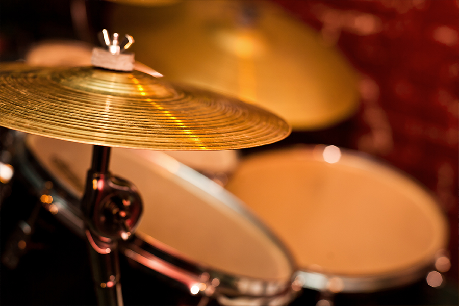 Close-up of a cymbal and drum set with warm stage lighting in the background.