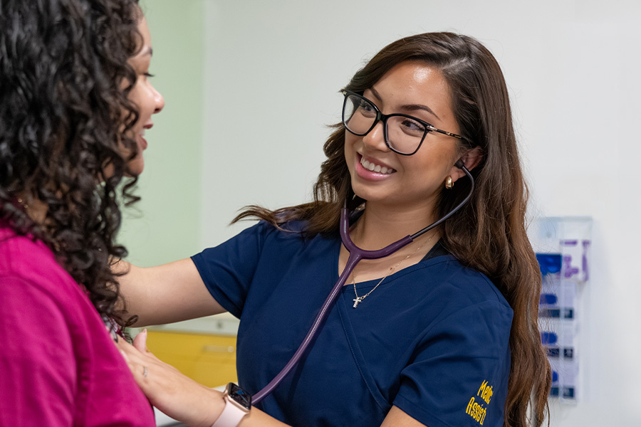 Medical assistant student in scrubs uses a stethoscope to listen to a patient's heartbeat