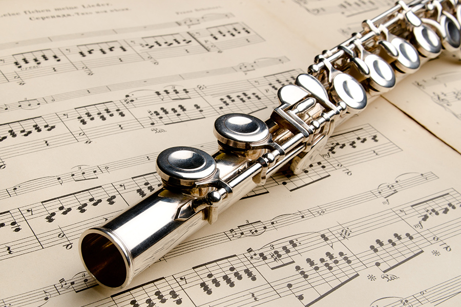 Close-up of a silver flute lying across printed sheet music.
